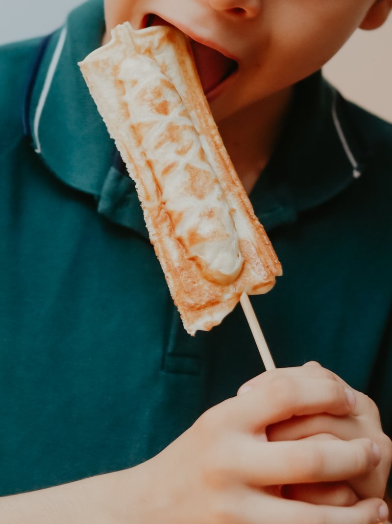 Menino mordendo um crepe suíço servido no palito