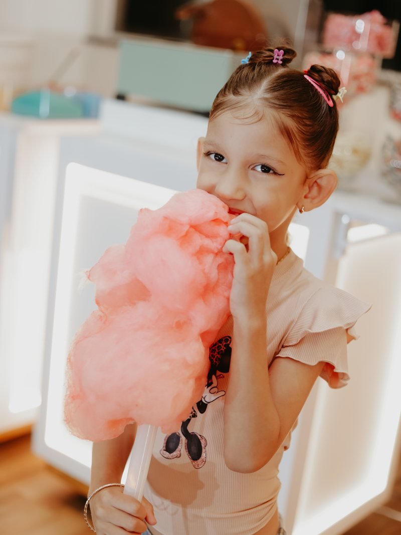 Menina comendo algodão-doce rosa ao lado do carrinho iluminado